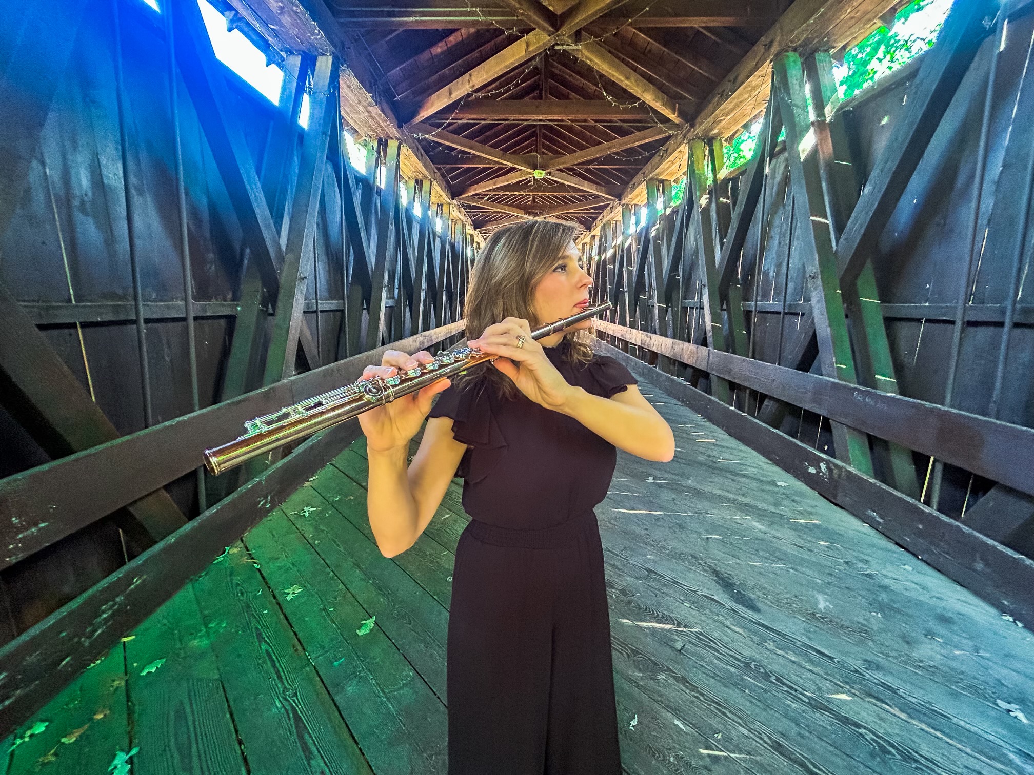 Abigail Walsh playing flute inside a covered wooden bridge.