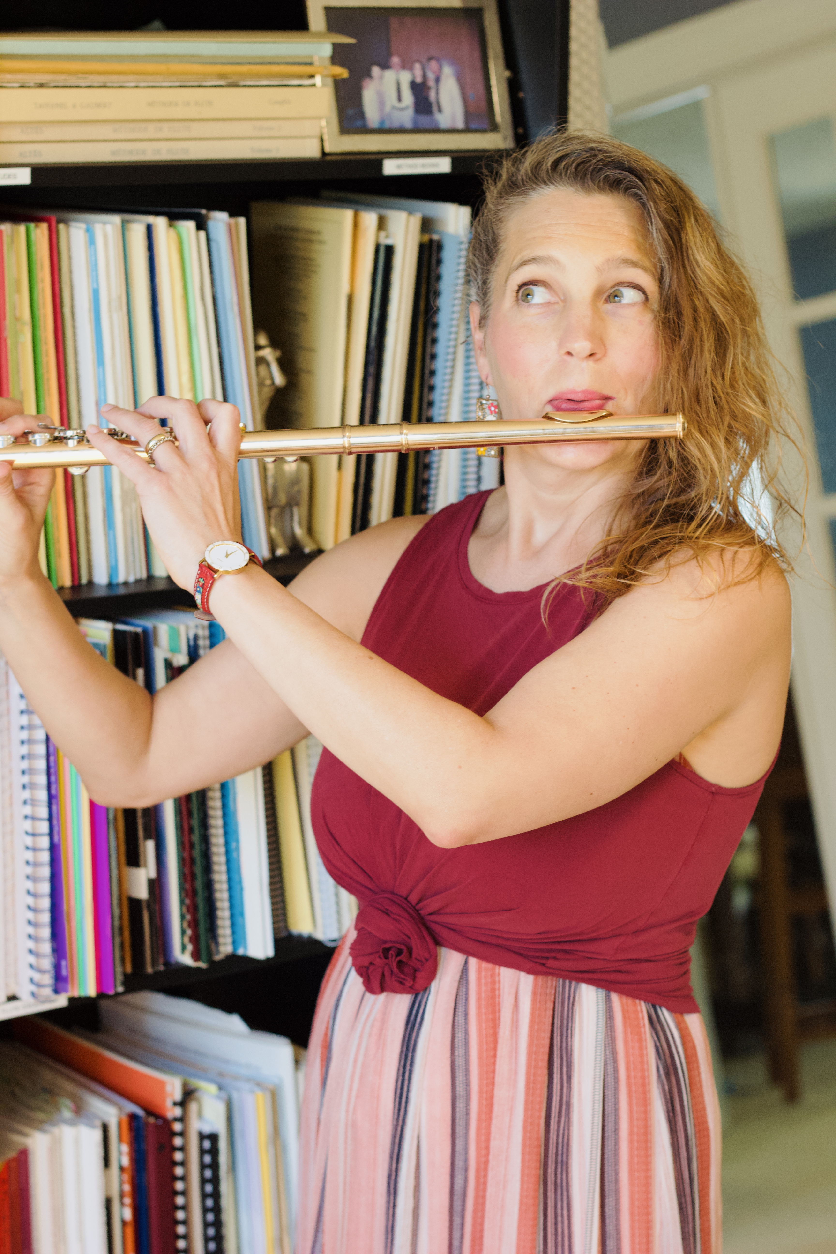 Abigail Walsh holding her flute and looking upward playfully in front of her music library.
