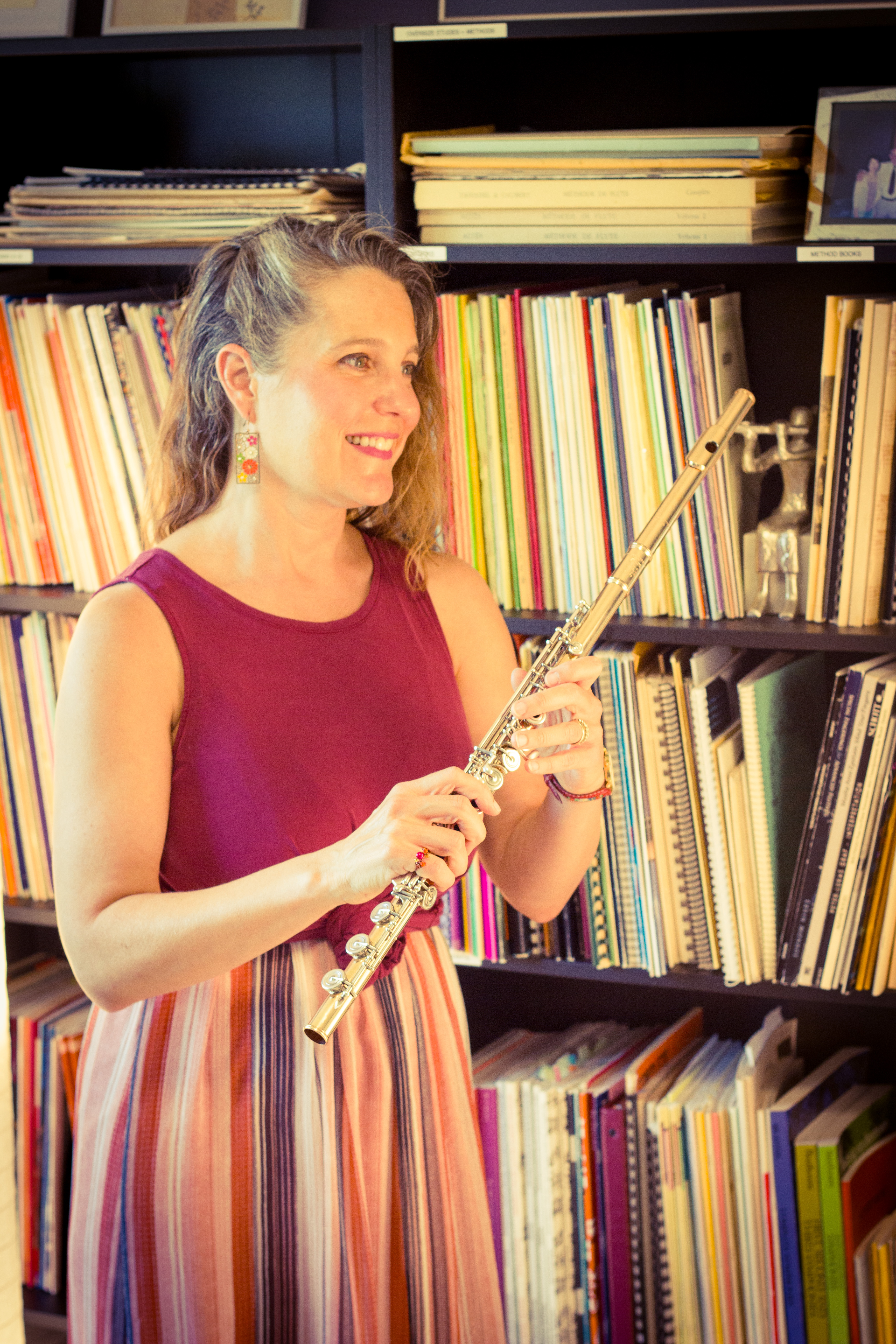 Abigail Walsh smiling and holding her flute in front of her music library.